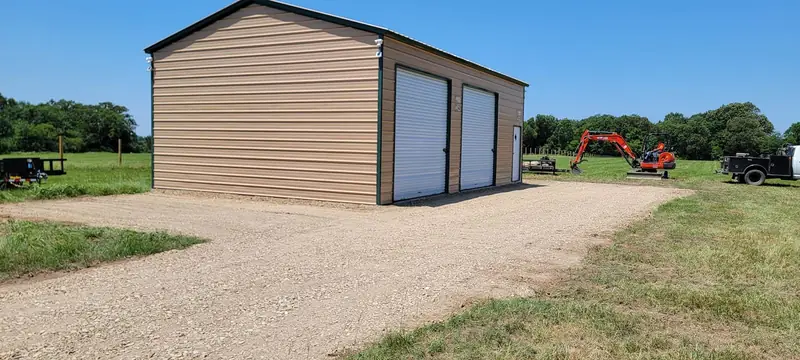 New gravel driveway leading to a tan metal shop building with roll-up doors