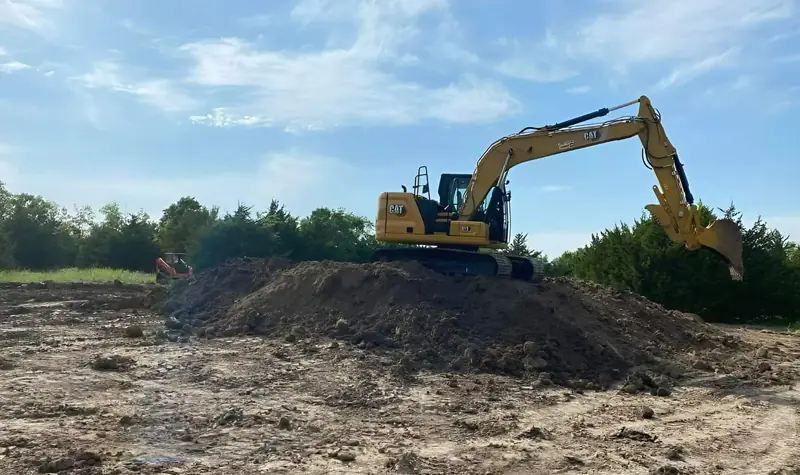 Excavator working on top of a large dirt pile at a cleared site