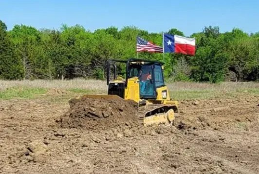 Circle H dozer flying the American and Texas flags while pushing dirt in a cleared field
