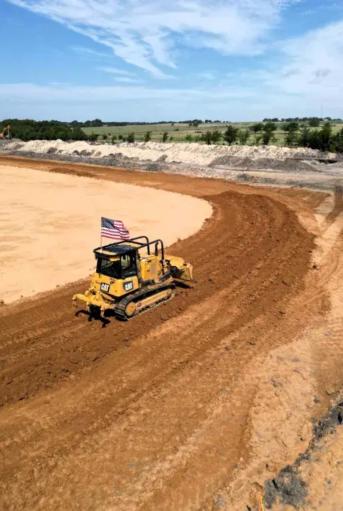 Dozer cutting and leveling a curved red dirt pad