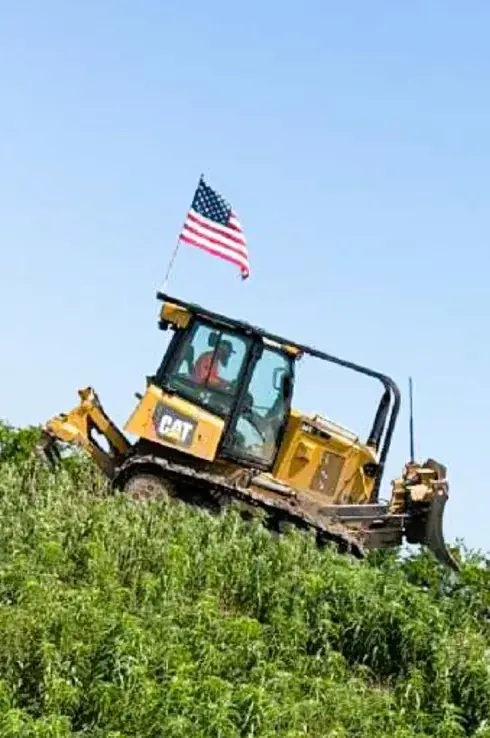 Dozer with an American flag working at the top of a grassy slope