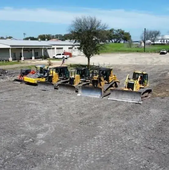 Fleet of dozers lined up on a gravel pad in front of a commercial building