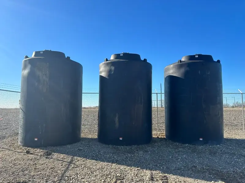 Three black water storage tanks set on a gravel pad