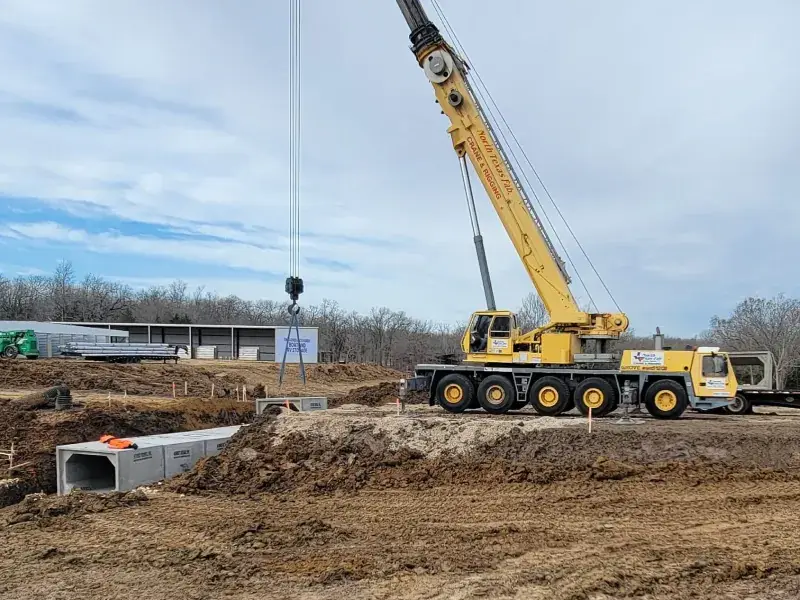 Crane on a construction site with a precast concrete section staged nearby