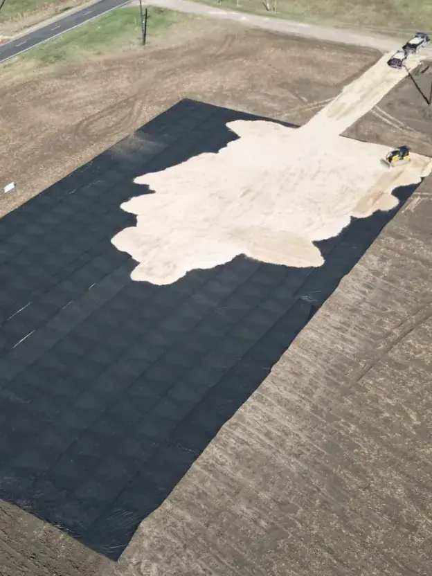 Aerial view of black ground cover laid over a graded area, with light rock spread across part of it