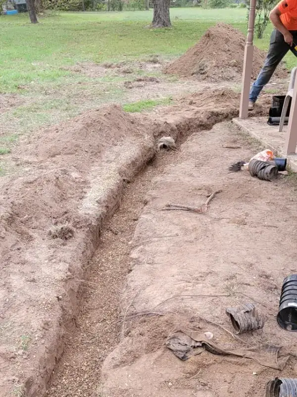 Trench dug through a yard with pipe fittings nearby