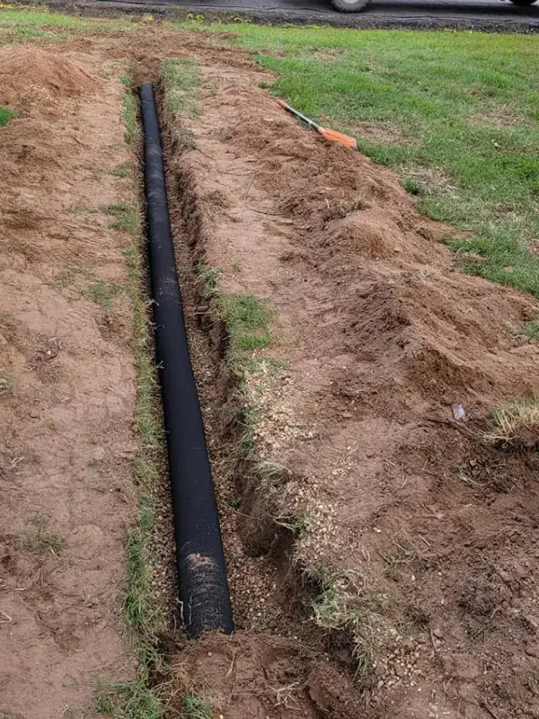 Black drain pipe laid in a trench through a grassy yard