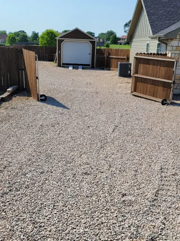 Gravel driveway and parking area beside a garage and fence