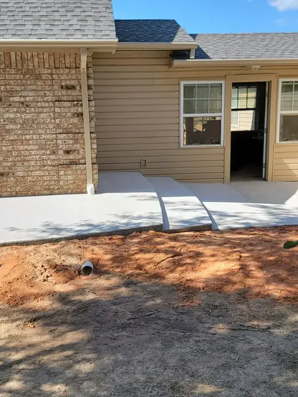 Dirt graded away from a home foundation beside a new concrete walk