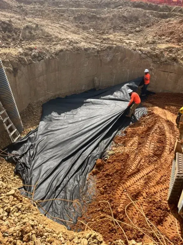 Crew spreading black plastic sheeting inside a large circular pit with concrete walls